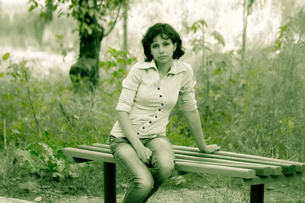 Dívka na lavičce v zelené pozadí — Stock fotografie