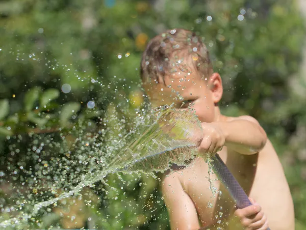 Junge spritzt Wasser aus Schlauch — Stockfoto
