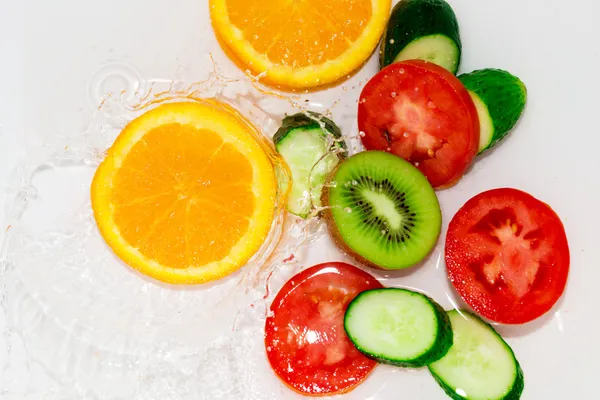 Свежие фрукты и овощи в воде на белом фоне — стоковое фото