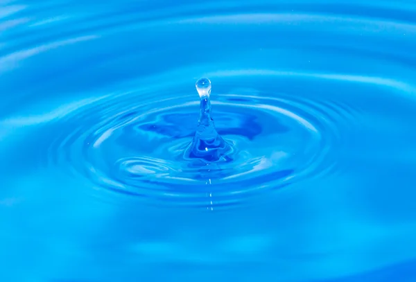 Uma gota de água caindo na água azul — Fotografia de Stock
