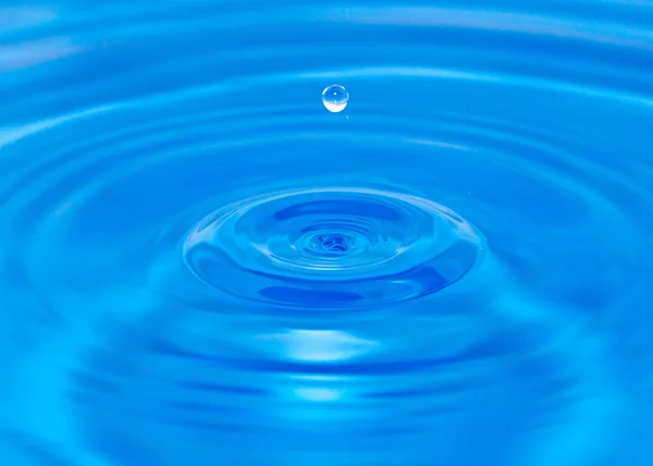 Uma gota de água caindo na água azul — Fotografia de Stock