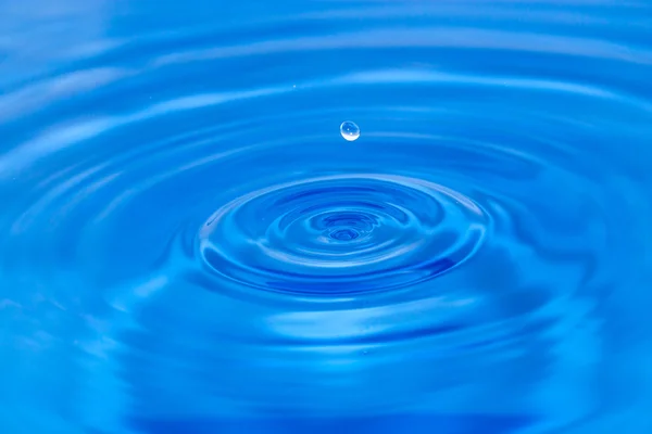 Uma gota de água caindo na água azul — Fotografia de Stock