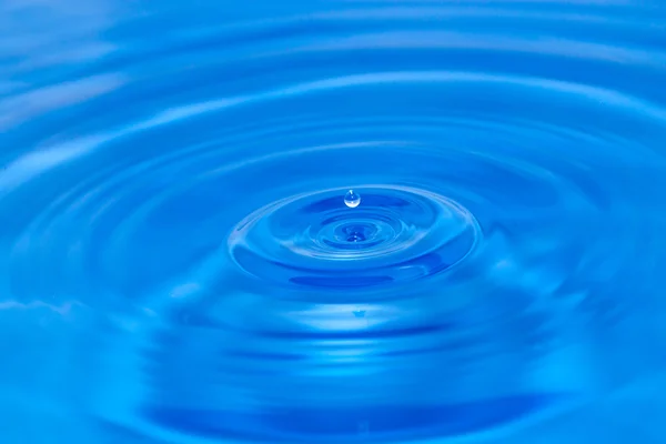 En droppe vatten falla i blått vatten — Stockfoto