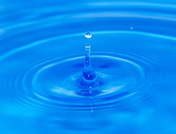 Uma gota de água caindo na água azul — Fotografia de Stock