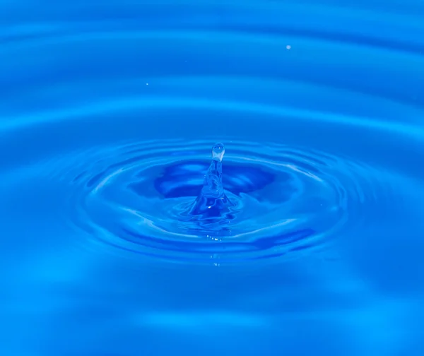 Uma gota de água caindo na água azul — Fotografia de Stock