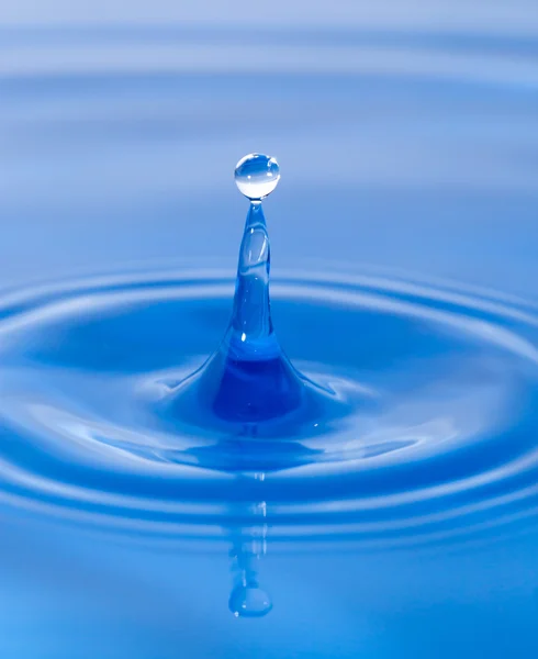 Uma gota de água caindo na água azul — Fotografia de Stock