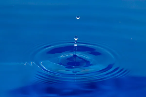 Een druppel water vallen in blauwe water — Stockfoto