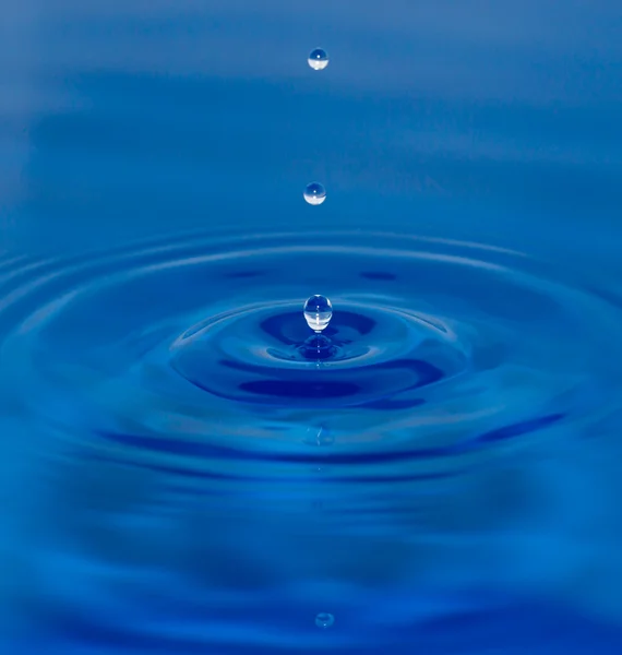 Una gota de agua cayendo en agua azul — Foto de Stock