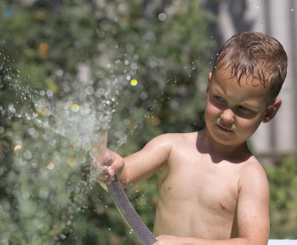 Junge spritzt Wasser aus Schlauch — Stockfoto