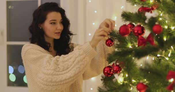 Frau schmückt Weihnachtsbaum zu Hause mit Weihnachtsbaumspielzeug — Stockvideo