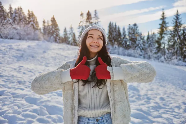 Mujer con ropa de invierno pulgares hacia arriba en frente del bosque de montaña al aire libre —  Fotos de Stock