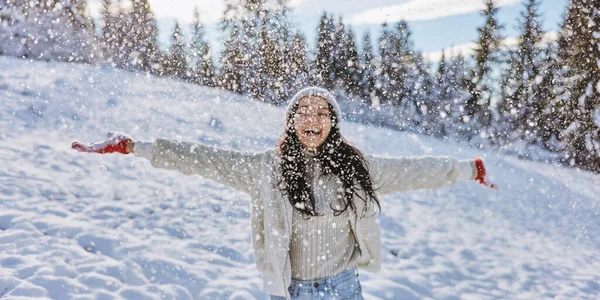 Mujer con ropa de invierno arrojando nieve al aire libre en el bosque —  Fotos de Stock