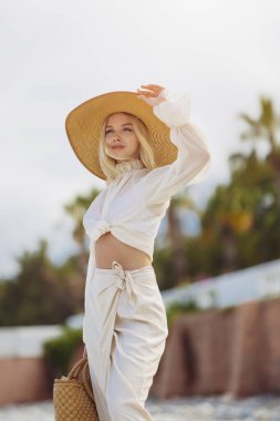 Yaz tatili boyunca arka planda palmiye ağaçlarına karşı şık plaj kıyafeti giyen kadın.