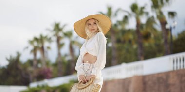 Yaz tatili boyunca arka planda palmiye ağaçlarına karşı şık plaj kıyafeti giyen kadın.