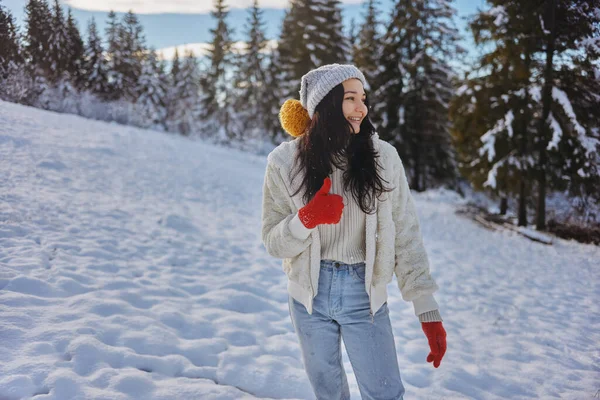 Mujer con ropa de invierno pulgares hacia arriba en frente del bosque de montaña al aire libre —  Fotos de Stock