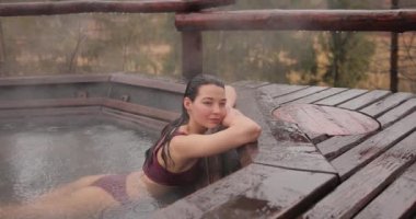 Bikinili bir kadın dışarıda ahşap bir banyoda banyo yapıyor.