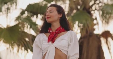 Yaz tatili boyunca arka planda palmiye ağaçlarına karşı şık plaj kıyafeti giyen kadın.