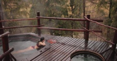 Bikinili bir kadın dışarıda ahşap bir banyoda banyo yapıyor.