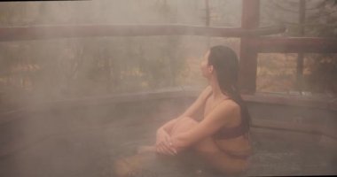 Bikinili bir kadın dışarıda ahşap bir banyoda banyo yapıyor.