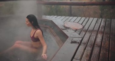 Bikinili bir kadın dışarıda ahşap bir banyoda banyo yapıyor.