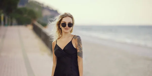 Femme blonde en robe noire en plein air contre le bord de la mer sur le fond pendant les vacances d'été à la plage — Photo