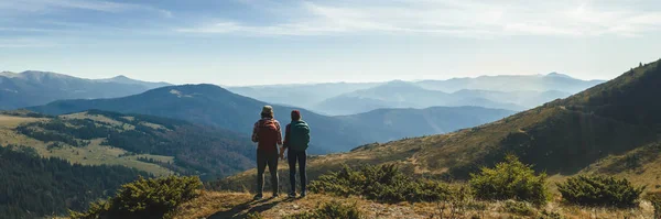 Casal de caminhantes com mochilas na frente da vista do vale da paisagem no topo de uma montanha — Fotografia de Stock