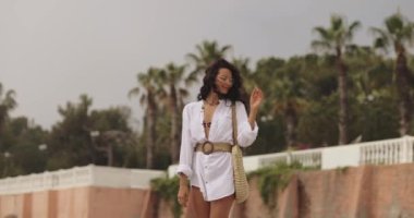 Yaz tatili boyunca arka planda palmiye ağaçlarına karşı şık plaj kıyafeti giyen kadın.