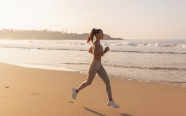 Koşan kadın. Kadın koşucu plajda dışarıda antrenman yaparken koşuyor. Açık havada çok güzel bir fitness modeli. Yüksek kalite fotoğraf