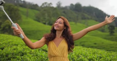 Selfie taking on Smartphone of Traveler Woman During Her Travel on Famous Nature Landmark Tea Plantations in Sri Lanka. Fashion model outdoor photographing her self on cell phone camera. High quality