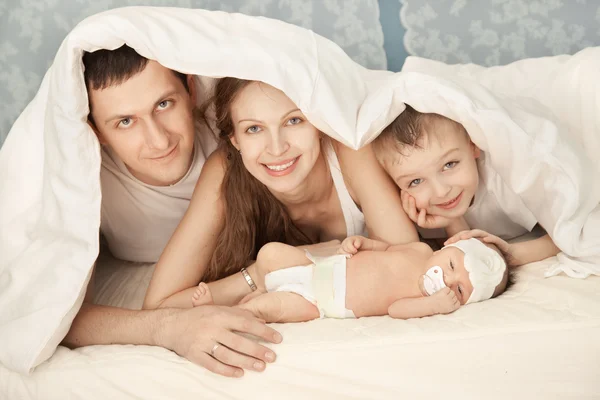 Uma família feliz na cama branca no quarto — Fotografia de Stock