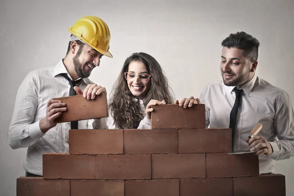 Businessmen and a business woman building a wall — Stock Photo, Image