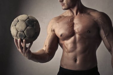 Futbol topu tutan genç kaslı adamın yakın çekimi.