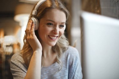 Bir kafede bilgisayar ve kulaklıkla genç bir kadın.