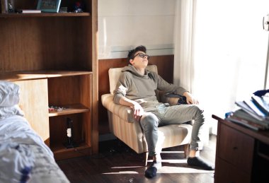 Sıkılmış genç bir çocuk yatak odasında bir koltukta oturuyor.