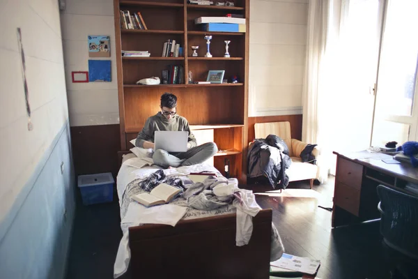 若い男は汚い寝室でノートパソコンを使い — ストック写真