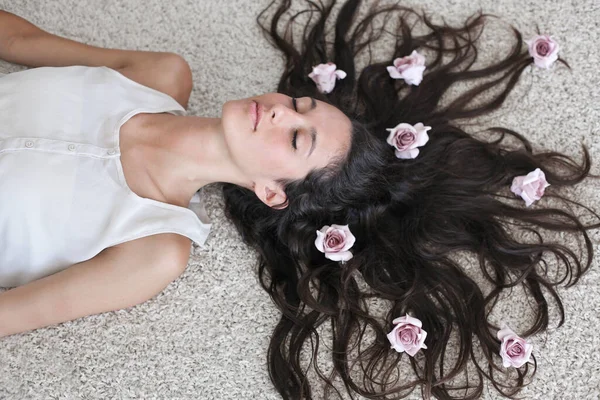 年轻的女人躺在床上 头发上插着小小的玫瑰 — 图库照片
