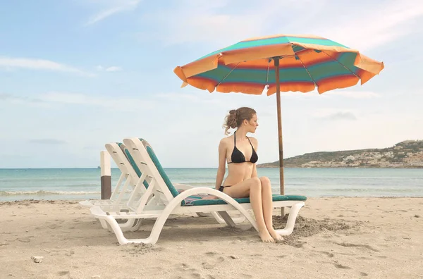 年轻女子坐在沙滩上的躺椅上 — 图库照片