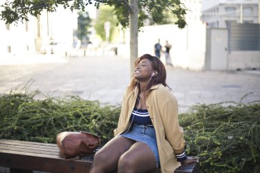 Genç siyahi kadın bankta müzik dinliyor.