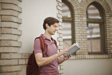 Genç adam sırtında sırt çantasıyla ders çalışıyor.