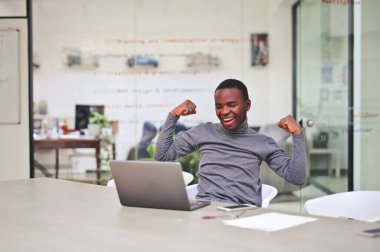 Genç, neşeli adam ofisteki bilgisayarın önünde seviniyor.