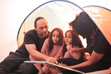 Aile, kamp çadırında resimli bir kitaba bakar.