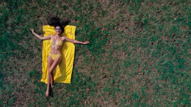 Genç ve güzel bir kadın bikinili çimlerin üzerinde yatıyor.