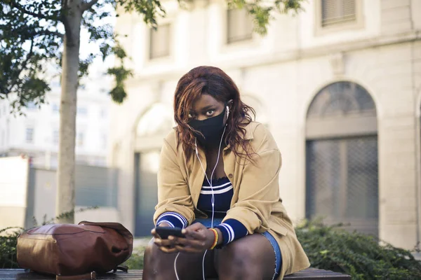 Junge Frau Mit Maske Sitzt Auf Einer Bank Und Hört — Stockfoto