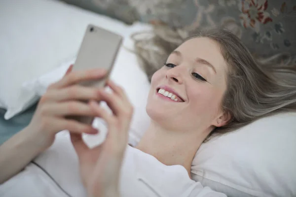 Jonge Vrouw Liggend Het Bed Schrijft Met Smartphone — Stockfoto