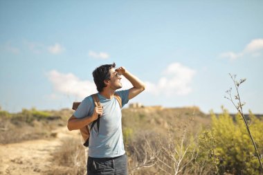 Sırt çantalı genç adam kırsalda yürüyor.