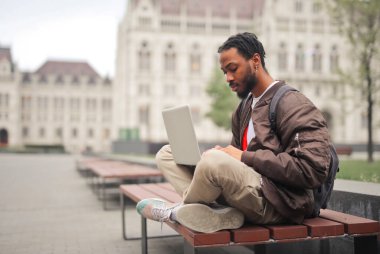 Şehirdeki bankta bilgisayarlı genç bir adam.