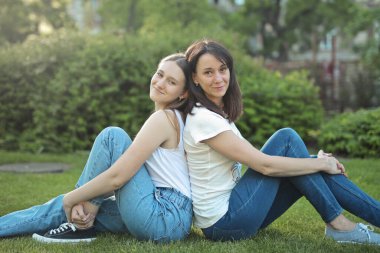 Anne ve kızı parkta çimlerin üzerinde oturuyor.