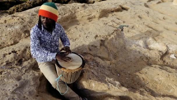 アフリカの打楽器音楽で セネガル人の男性が手で伝統的なジェムドラムを演奏します 西アフリカの伝統音楽は通りや祭りで演奏されることが多い モロッコのエサウイラのビーチで野外音楽 — ストック動画