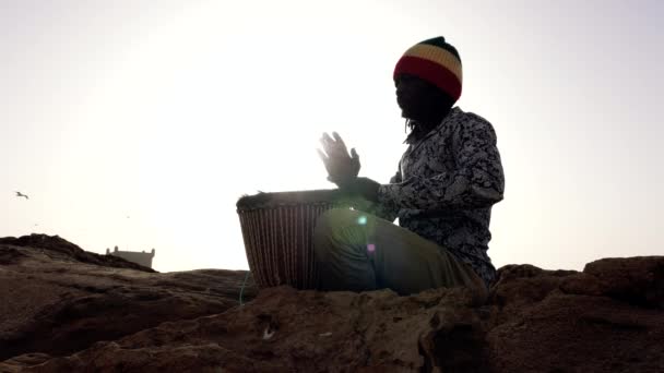 アフリカの打楽器音楽で セネガル人の男性が手で伝統的なジェムドラムを演奏します 西アフリカの伝統音楽は通りや祭りで演奏されることが多い 4Kバックライト — ストック動画