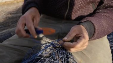 Bir balıkçı, Fas 'ın Essaouira limanında mavi bir balıkçı ağını iplikle onarıyor. Kırsal liman manzarası.